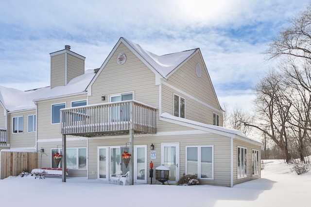 snow covered rear of property featuring a balcony, a chimney, and fence