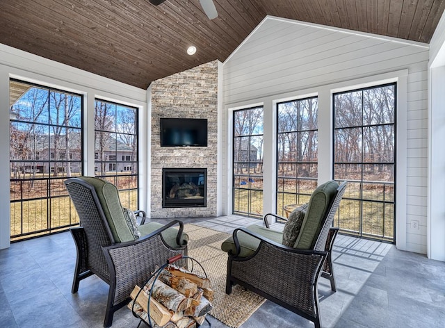 sunroom / solarium featuring lofted ceiling, wooden ceiling, ceiling fan, and a stone fireplace