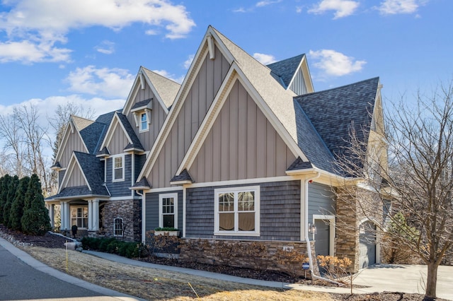 shingle-style home with stone siding, a shingled roof, board and batten siding, and concrete driveway