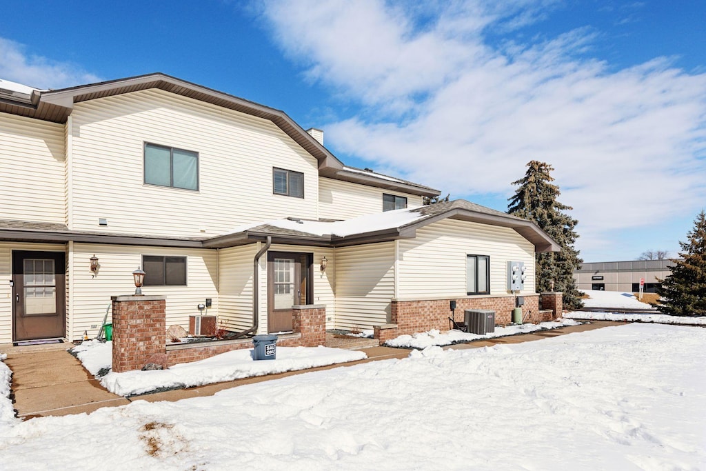 snow covered back of property with cooling unit and brick siding