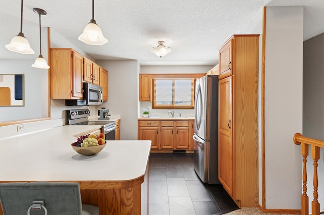 kitchen with a peninsula, a sink, hanging light fixtures, light countertops, and appliances with stainless steel finishes