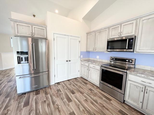 kitchen with light wood-style floors, vaulted ceiling, light stone counters, and stainless steel appliances