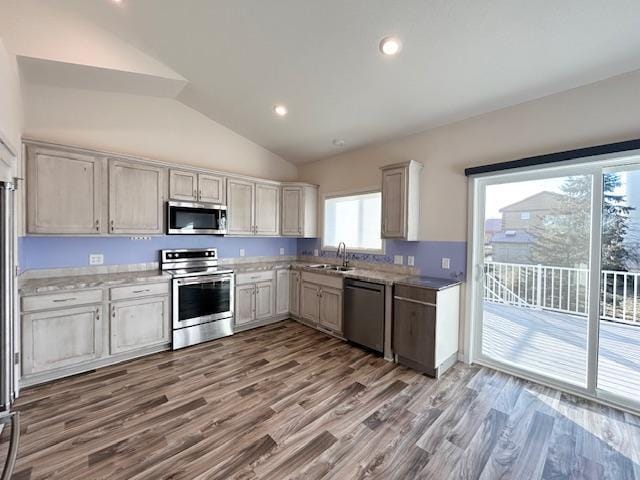 kitchen with lofted ceiling, recessed lighting, stainless steel appliances, wood finished floors, and a sink