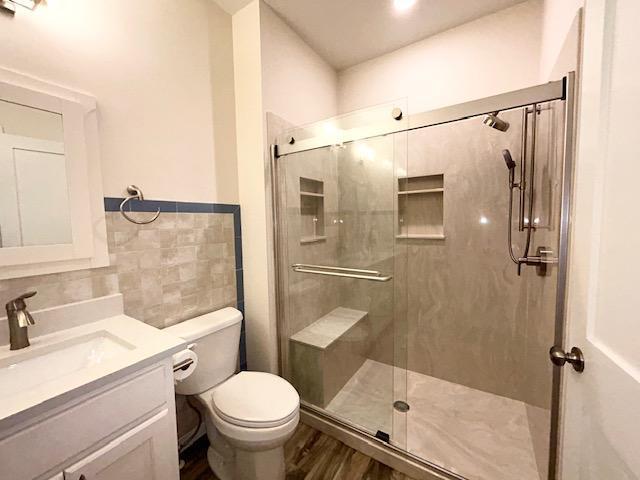 full bathroom featuring tile walls, toilet, a stall shower, vanity, and wood finished floors