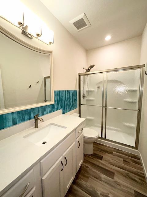 full bathroom with toilet, wood finished floors, vanity, visible vents, and a stall shower