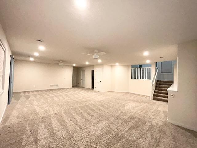 finished basement featuring ceiling fan, stairway, and carpet