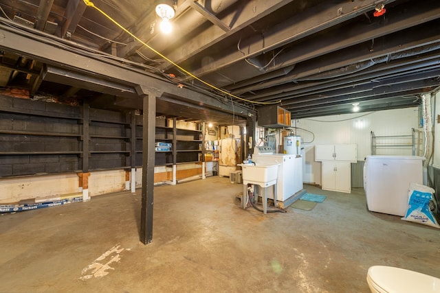 basement featuring fridge, washer and clothes dryer, and water heater