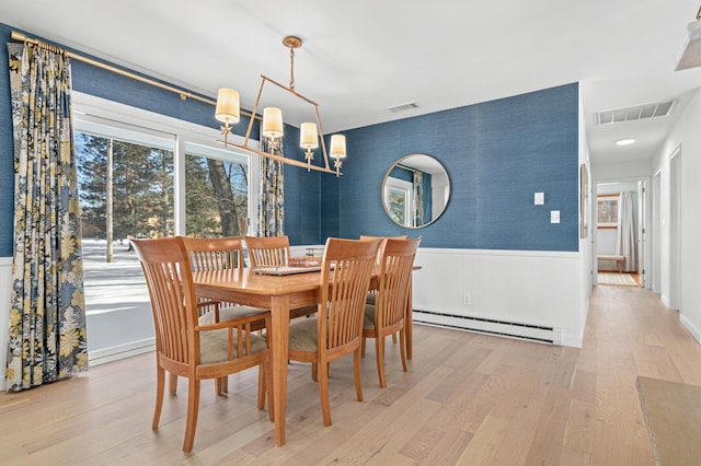 dining space with light wood-style floors, a baseboard radiator, a wainscoted wall, and visible vents