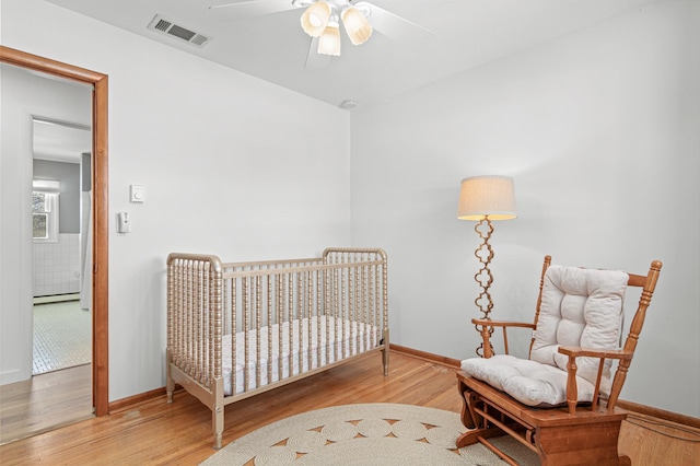 bedroom featuring a baseboard heating unit, baseboards, visible vents, and wood finished floors