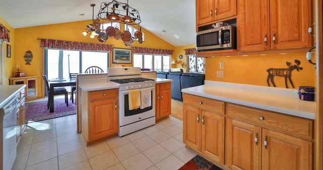 kitchen with light tile patterned floors, light countertops, appliances with stainless steel finishes, brown cabinetry, and vaulted ceiling