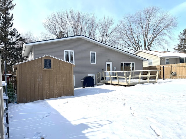 snow covered rear of property featuring a storage unit and a wooden deck