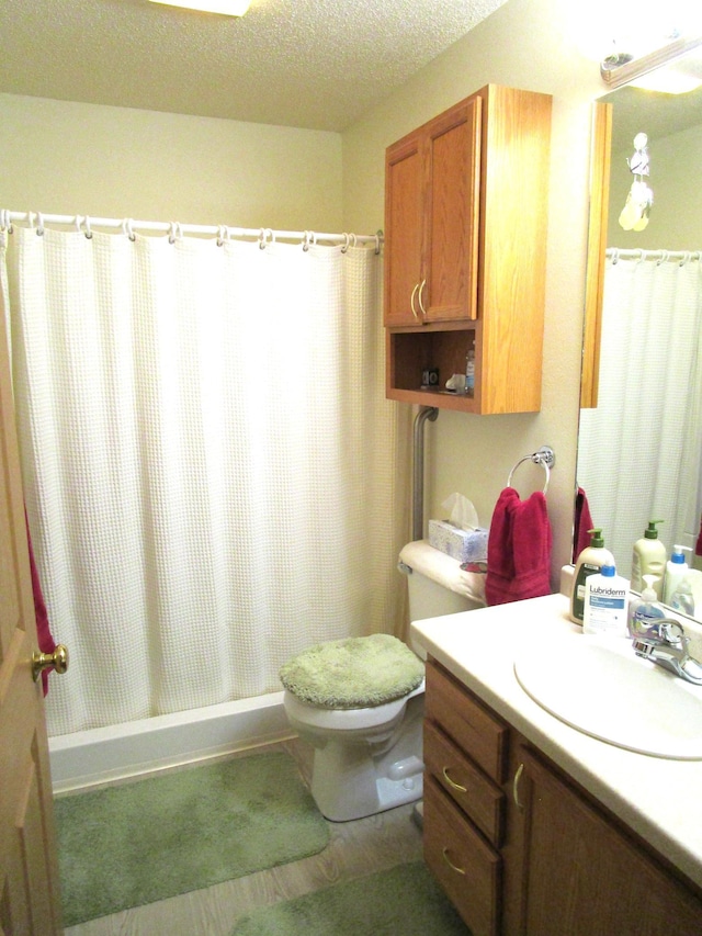 bathroom featuring walk in shower, vanity, toilet, and a textured ceiling