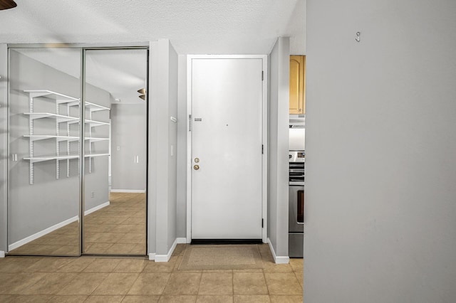 interior space featuring light tile patterned floors, a textured ceiling, and baseboards
