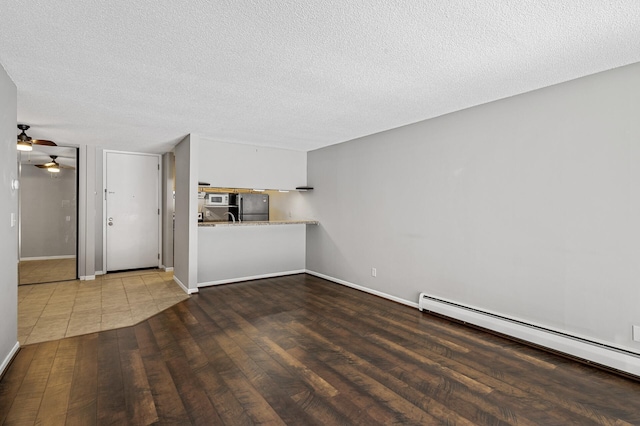 unfurnished living room with a textured ceiling, a ceiling fan, wood finished floors, a baseboard radiator, and baseboards