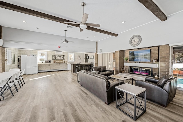 living room featuring light wood-type flooring, beamed ceiling, a ceiling fan, and a glass covered fireplace