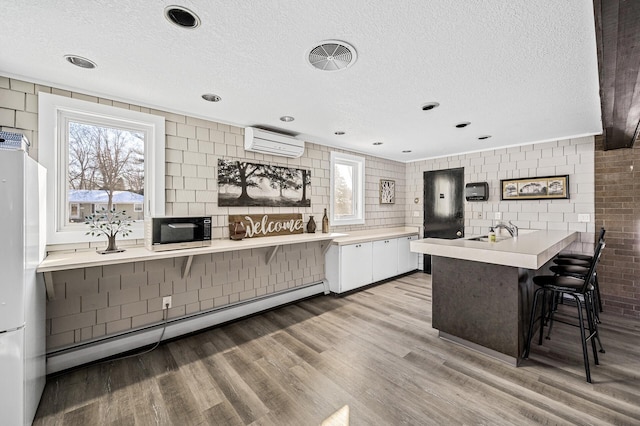 kitchen featuring an AC wall unit, plenty of natural light, freestanding refrigerator, light wood finished floors, and a baseboard radiator