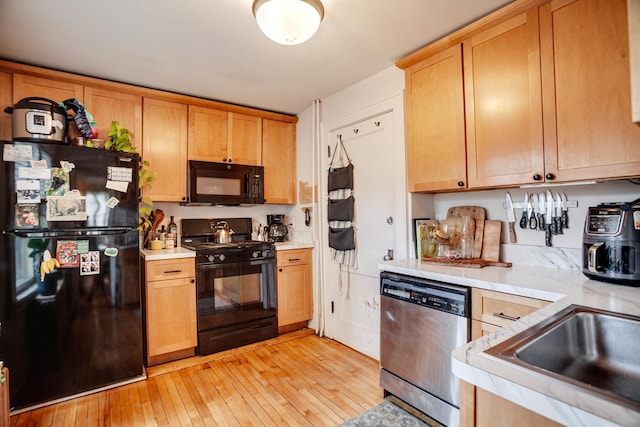 kitchen with black appliances, light countertops, light wood finished floors, and a sink