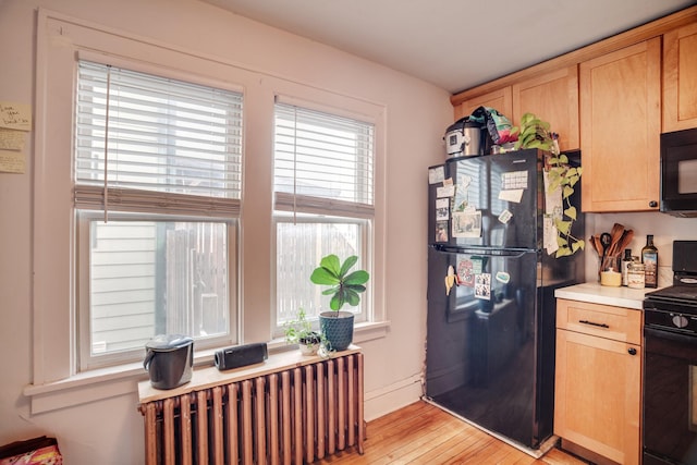 kitchen with light wood finished floors, light brown cabinets, radiator heating unit, light countertops, and black appliances