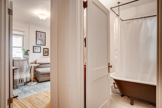 bathroom with a shower with shower curtain, wood finished floors, and a freestanding bath