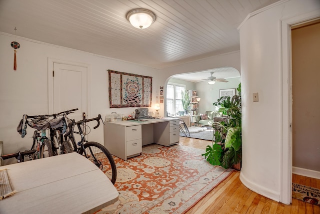 interior space with baseboards, arched walkways, crown molding, and light wood finished floors