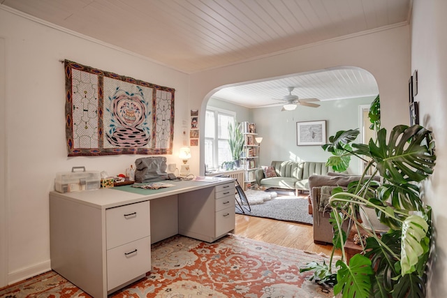 home office featuring light wood-type flooring, a ceiling fan, arched walkways, and ornamental molding