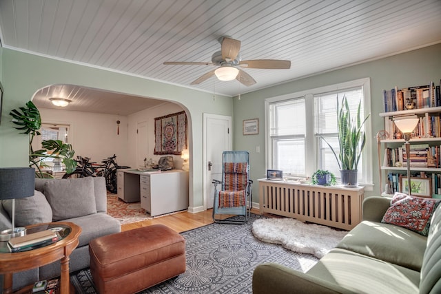 living room featuring radiator, a ceiling fan, arched walkways, crown molding, and light wood-type flooring