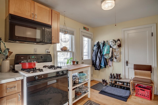 kitchen with light wood-type flooring, black microwave, light countertops, baseboards, and white gas range