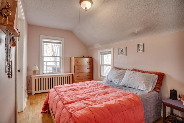 bedroom featuring lofted ceiling, radiator, light wood-type flooring, and a textured ceiling