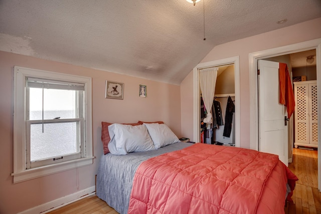 bedroom with wood finished floors, baseboards, vaulted ceiling, a closet, and a textured ceiling