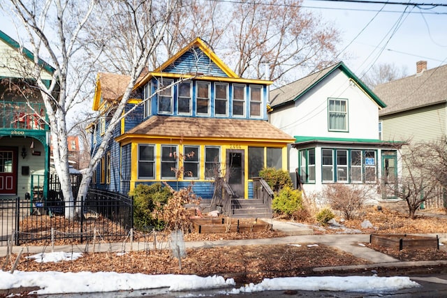 view of front of home with a shingled roof, a sunroom, and fence