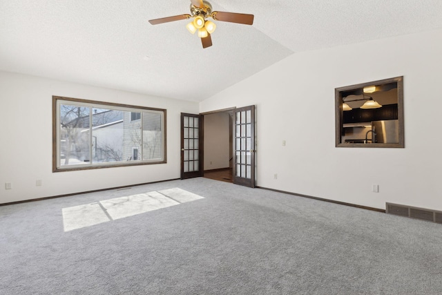 empty room with a textured ceiling, vaulted ceiling, light colored carpet, and ceiling fan