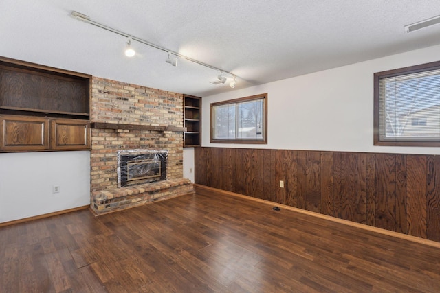 unfurnished living room with a textured ceiling, wooden walls, dark hardwood / wood-style floors, and a fireplace