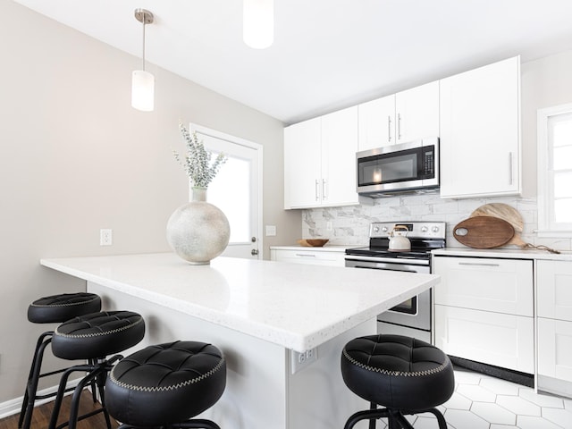 kitchen featuring a kitchen bar, appliances with stainless steel finishes, pendant lighting, white cabinets, and decorative backsplash