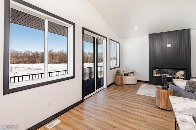 unfurnished living room featuring lofted ceiling, visible vents, a large fireplace, light wood-type flooring, and baseboards