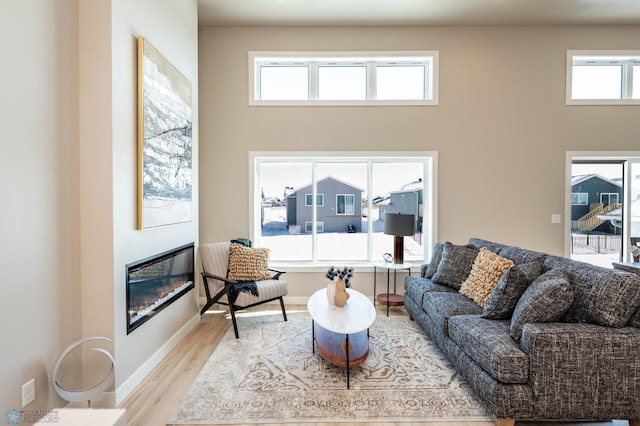 living area with light wood finished floors, baseboards, and a glass covered fireplace