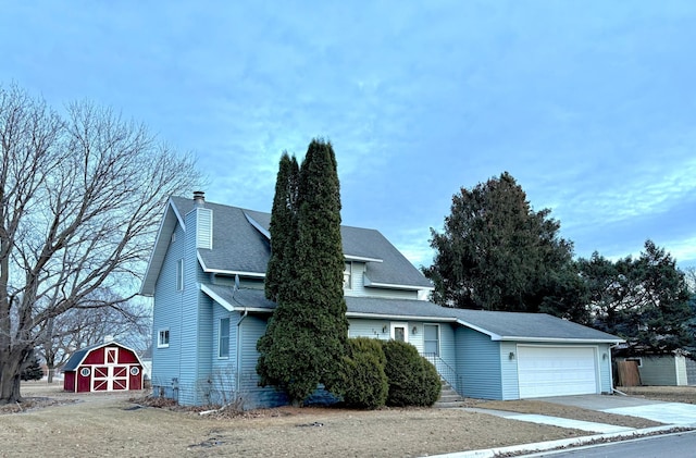 view of front of home featuring a barn, a shingled roof, driveway, an outbuilding, and an attached garage