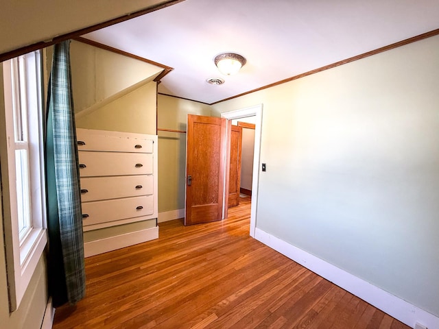 unfurnished bedroom with visible vents, crown molding, baseboards, and wood finished floors