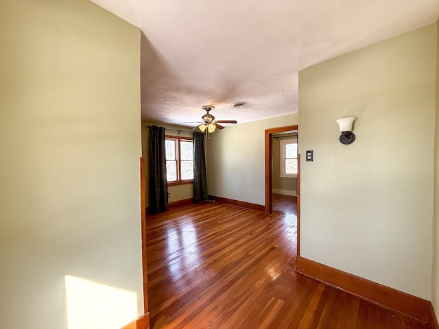 empty room with hardwood / wood-style floors, visible vents, baseboards, and ceiling fan