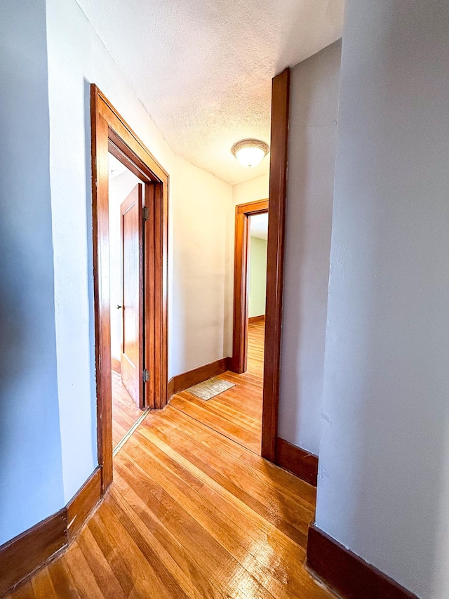 hall featuring a textured ceiling, light wood-type flooring, and baseboards