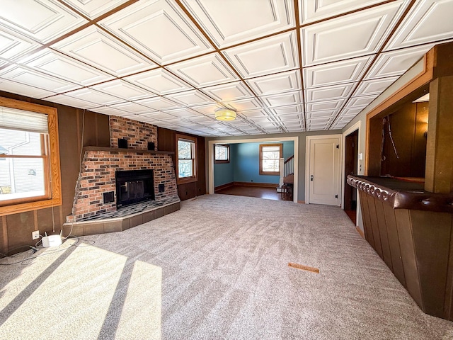 unfurnished living room with wooden walls, carpet, a fireplace, an ornate ceiling, and stairs