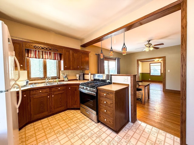 kitchen featuring light floors, a peninsula, freestanding refrigerator, stainless steel gas range, and a sink