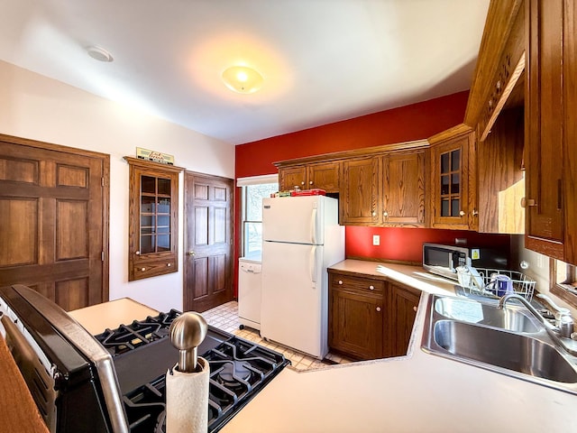 kitchen with glass insert cabinets, light countertops, brown cabinets, white appliances, and a sink