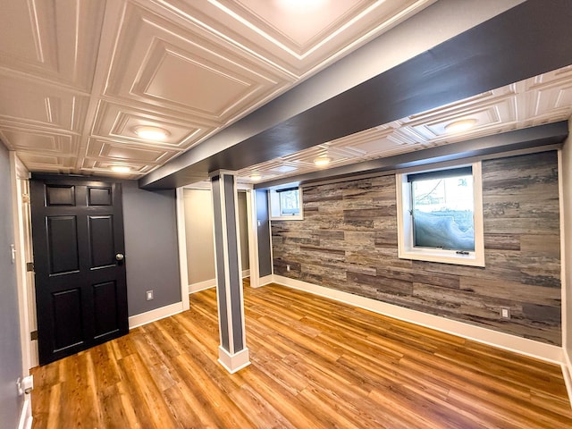 basement with wooden walls, baseboards, a wealth of natural light, light wood-style flooring, and an ornate ceiling