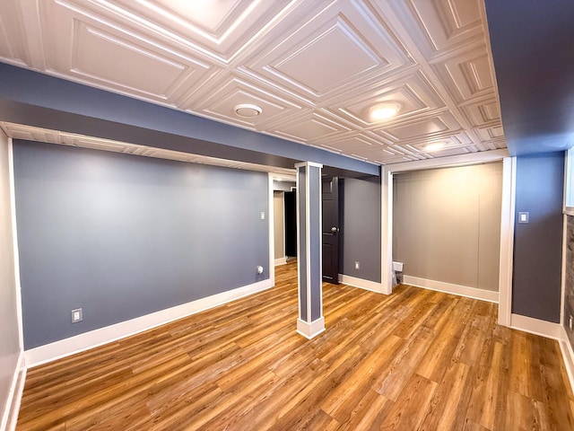 finished basement featuring baseboards, an ornate ceiling, and light wood finished floors