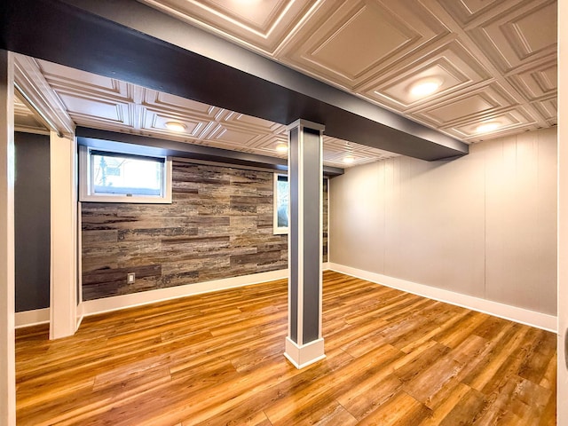 basement with light wood-type flooring, an ornate ceiling, wooden walls, and baseboards