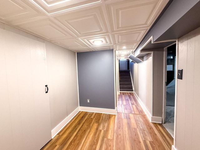 finished below grade area with stairway, light wood-style floors, baseboards, and an ornate ceiling