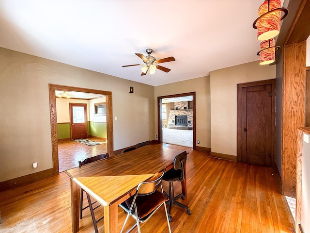 dining area featuring baseboards, a fireplace with raised hearth, light wood-type flooring, and ceiling fan