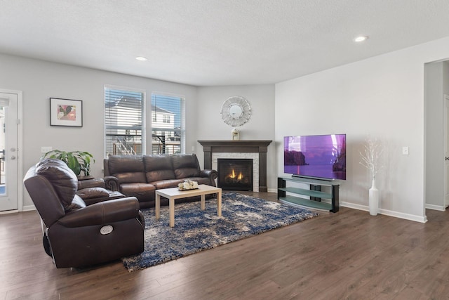 living room with a warm lit fireplace, dark wood-type flooring, a textured ceiling, and baseboards