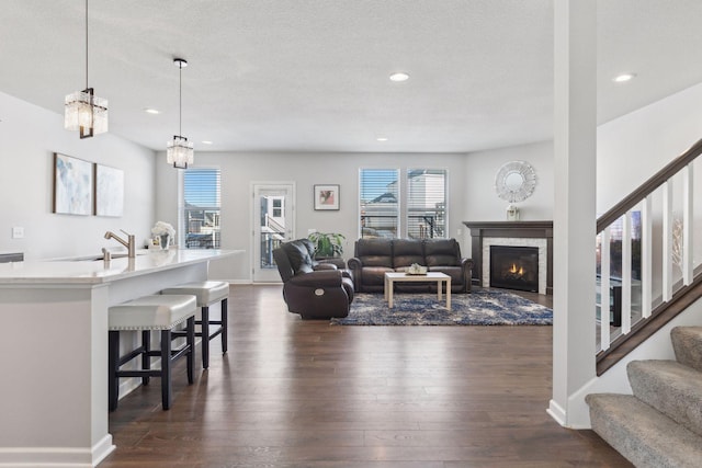 living area with stairs, a lit fireplace, dark wood finished floors, and recessed lighting