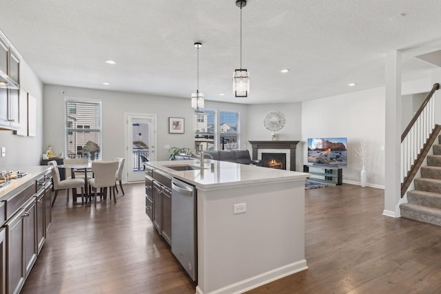 kitchen featuring an island with sink, a sink, light countertops, pendant lighting, and stainless steel dishwasher